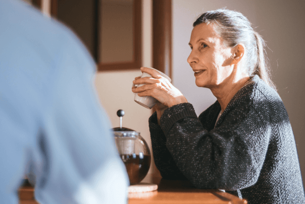 An older woman is smiling holding a cup of coffee