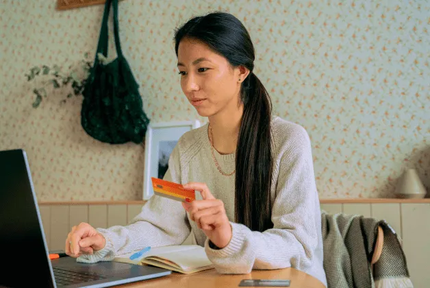 A young woman looks at her laptop with her credit card at the ready