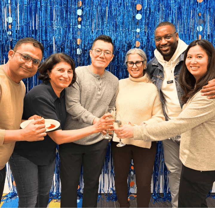 A collection of Fintel Connect employees against a wall of blue streamers, holding their hands in the middle with champagne glasses for a toast